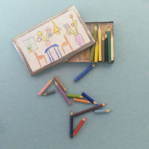 Een miniatuur kleurpotlodendoosje met een kindertekening op de deksel. Leuk detail: sommige kleurpotloodjes zijn aan het eind 'ingebeten'.